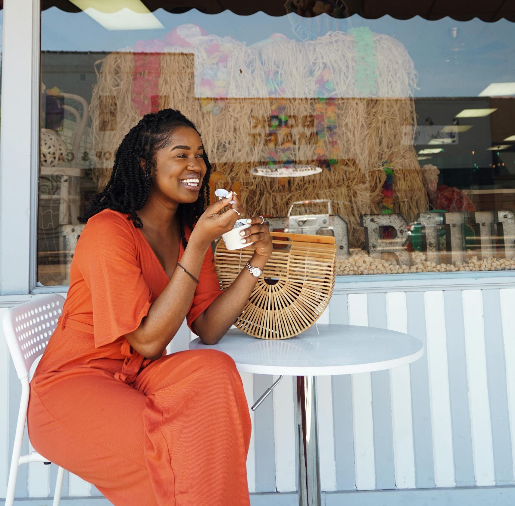 A smiling woman enjoys ice cream while sitting on a patio.