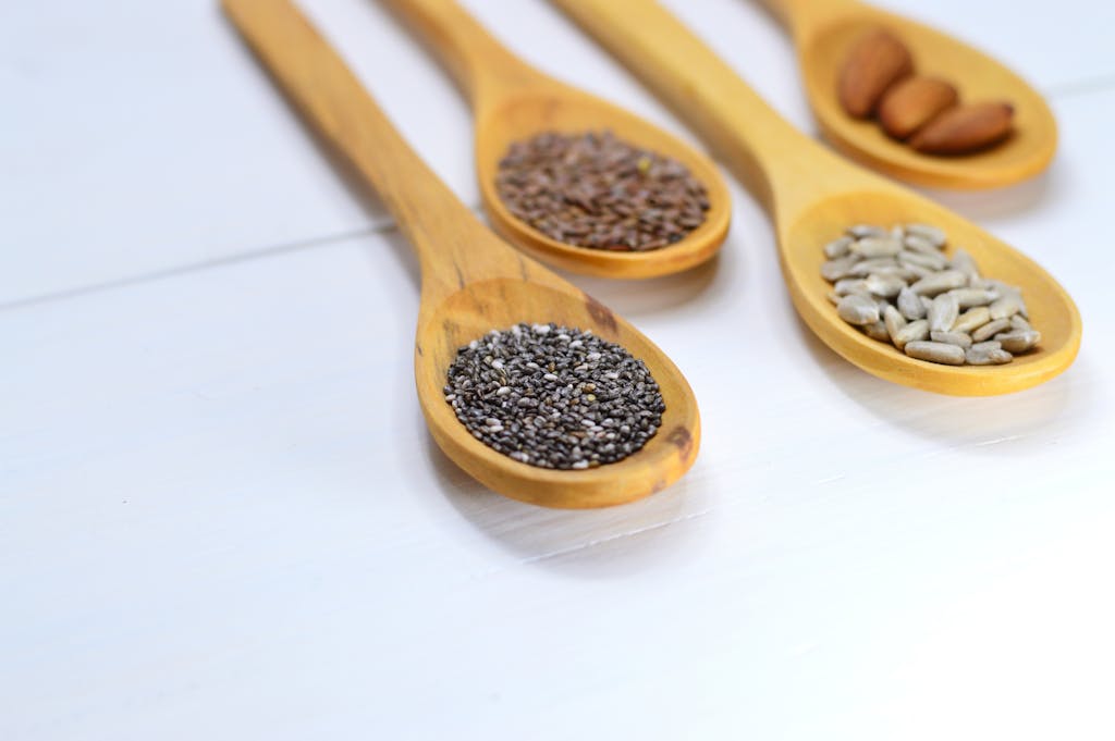 A variety of seeds and nuts in wooden spoons displayed on a white surface.