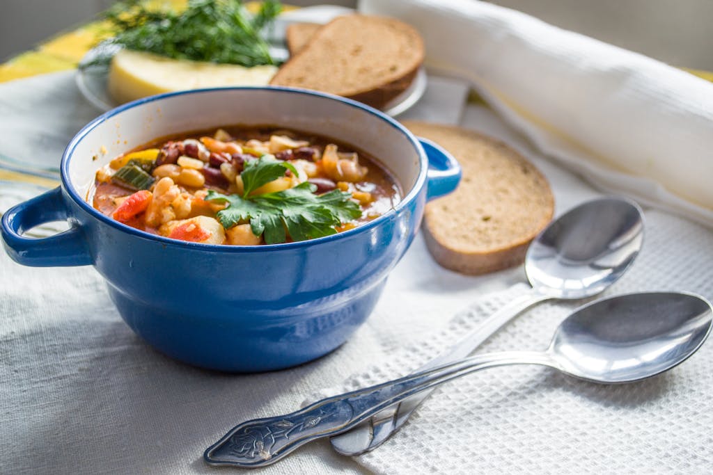 Colorful vegetable soup served in a blue ceramic bowl with bread slices on a cozy table setting.