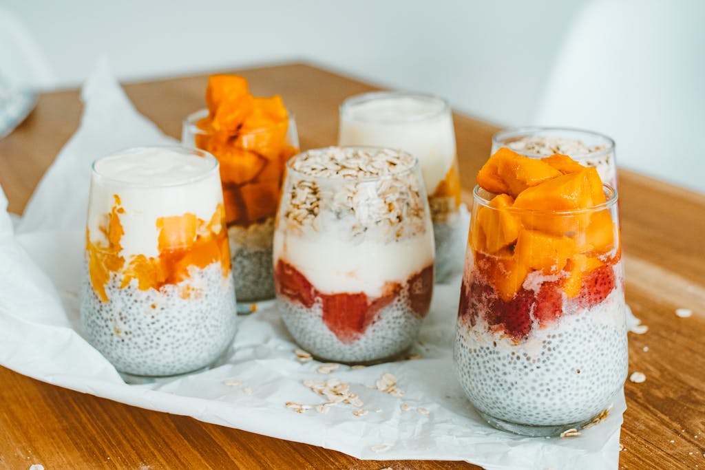 Delicious chia pudding parfaits with mango and strawberry layers on a wooden table.