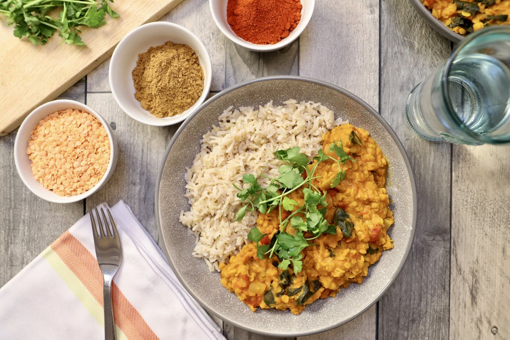 Flavorful vegan lentil curry served with rice, garnished with fresh herbs. A serving of lentils gives you your full daily recommended intake of soluble fiber, helping lower cholesterol levels.