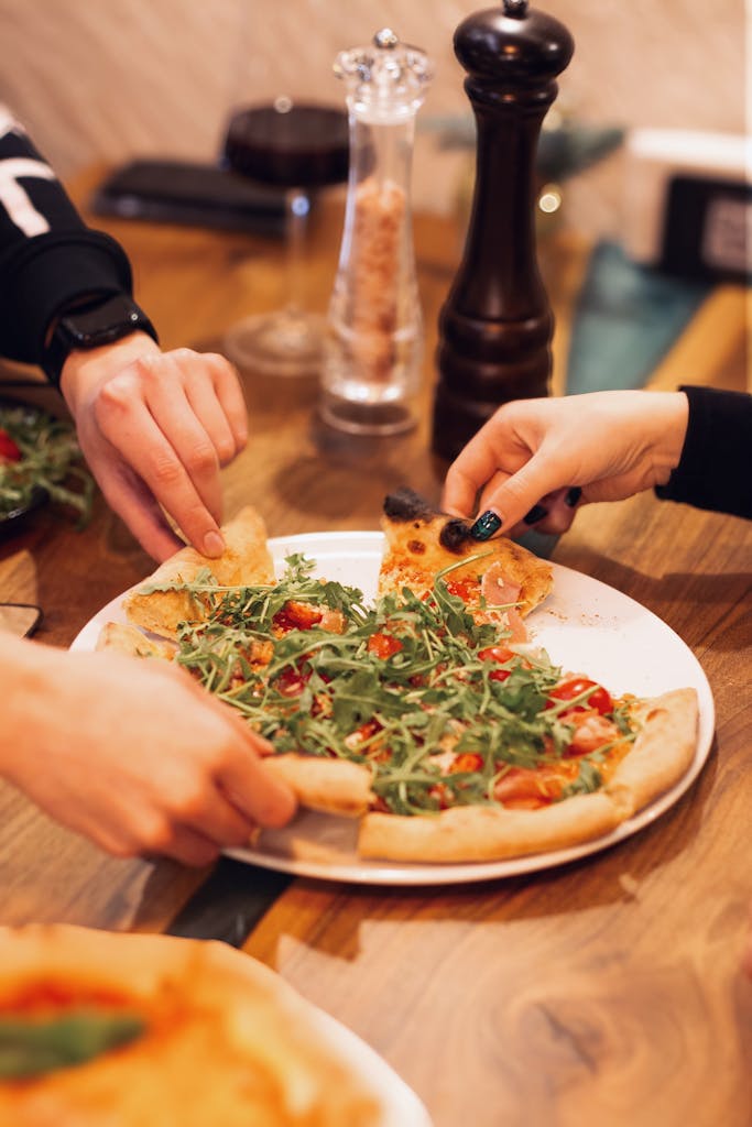 Three different hands reaching in to grab a slice of pizza symbolizing meals shared with friends. 