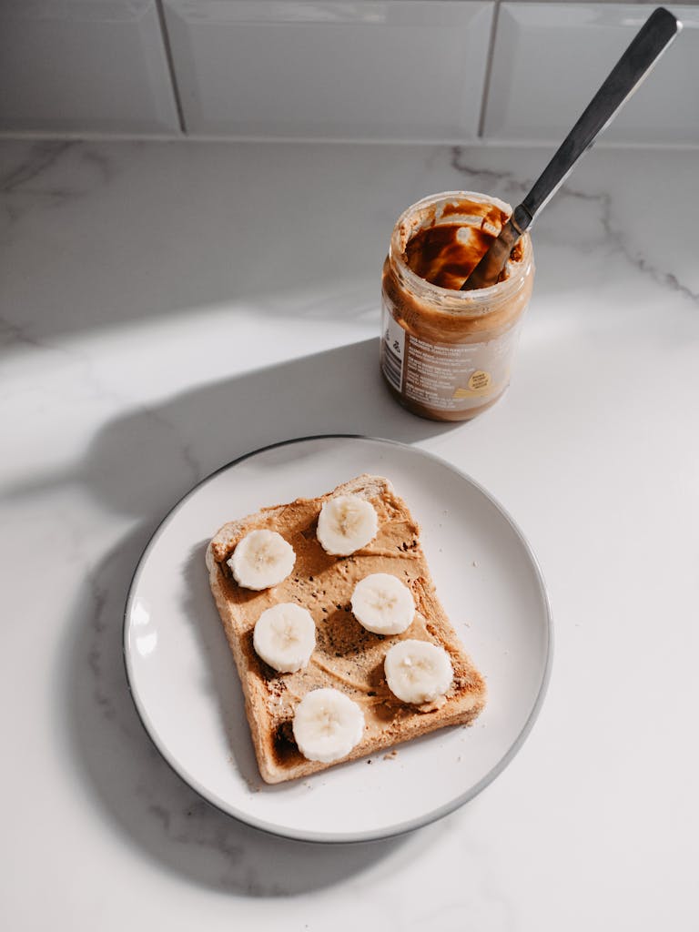 Sliced banana on peanut butter toast served on a white plate for quick meal or snack option when you don't have much of an appetite.