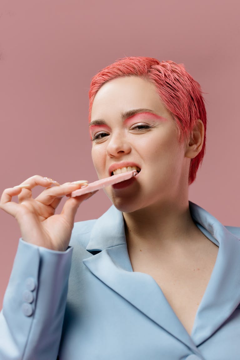 Stylish woman in blue suit, pink hair, indulging in a sweet treat. Modern portrait.