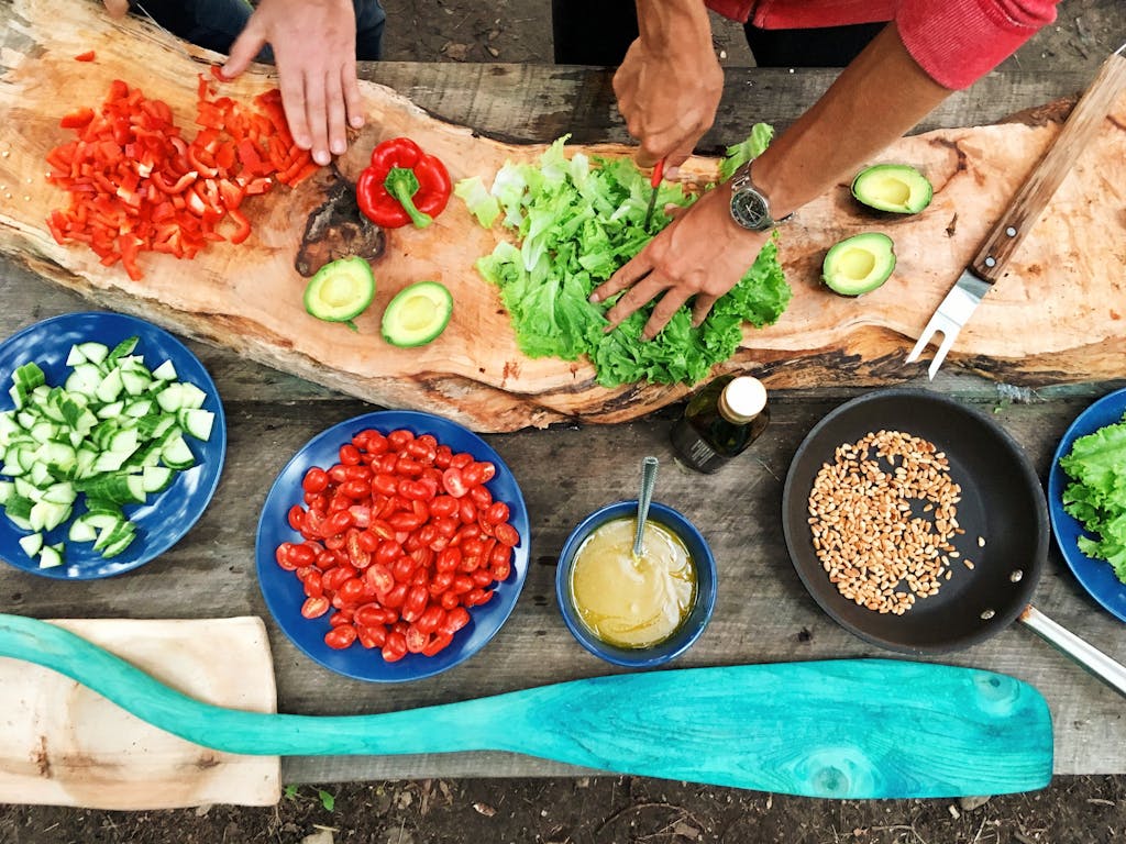 Two sets of hands cutting colorful vegetables, Pictured a variety of veggies, avocado and grains. Healthy eating for menopause includes a variety of whole grains, colorful vegetables, lean proteins.